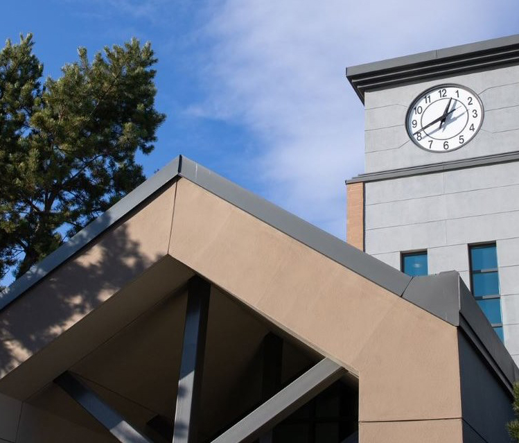 External photograph of the clock tower at Thompson Rivers University, set against a partly cloudy mid-day sky