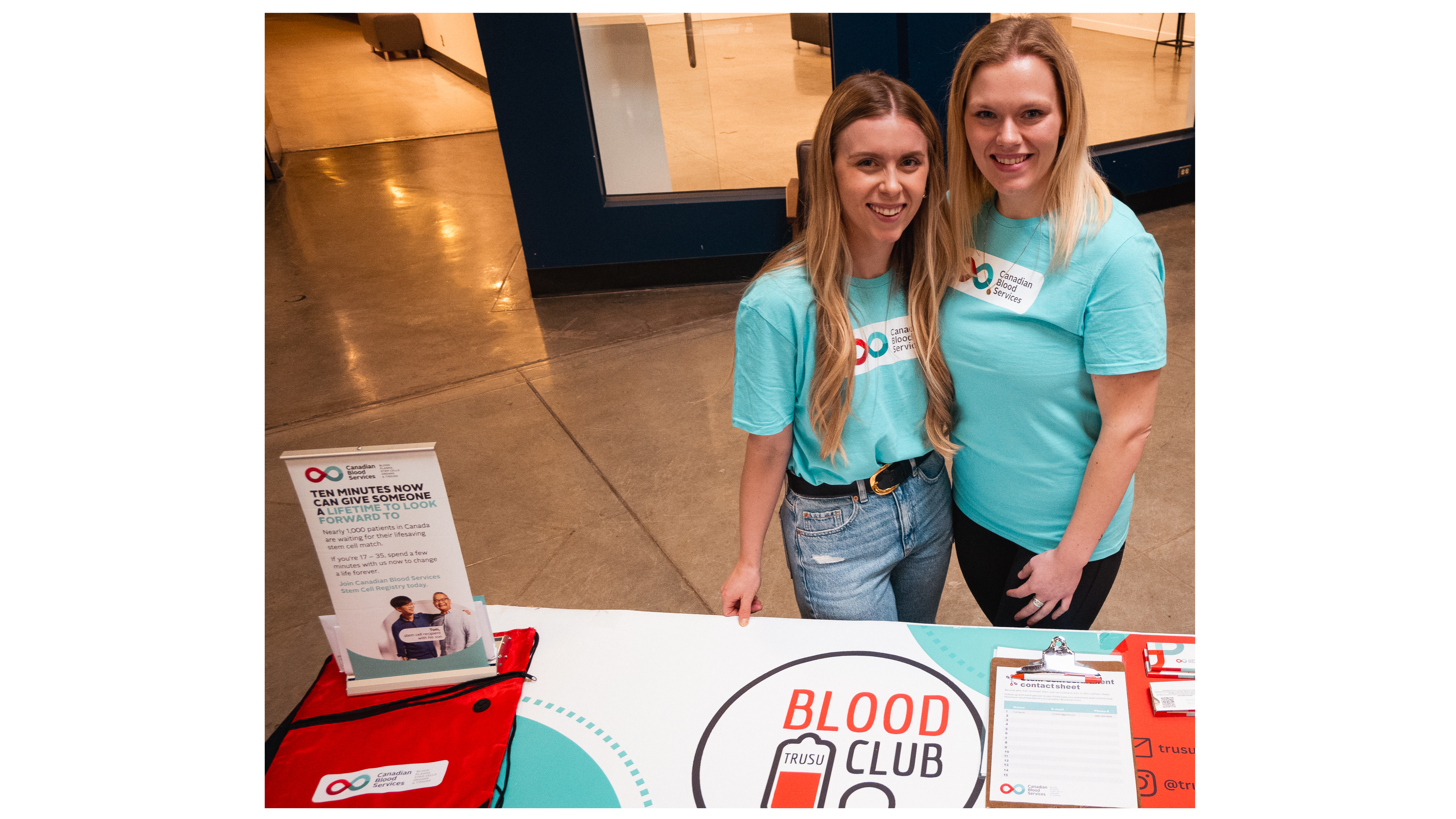Blood Club president, Emily Fagg stands on the left side of the picture with club vice-president Tess Russell for a table event in Old Main. Both women are wearing teal coloured shirts.