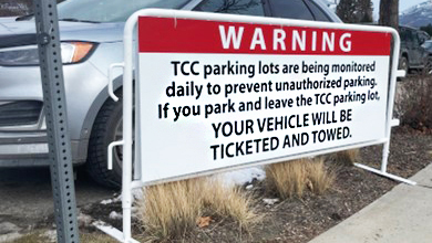 A white and red sign hanging on a white frame at the Tournament Capital Centre parking lot. The sign is advising that only patrons of the TCC are permitted to park in the lot, and all other vehicles will be towed